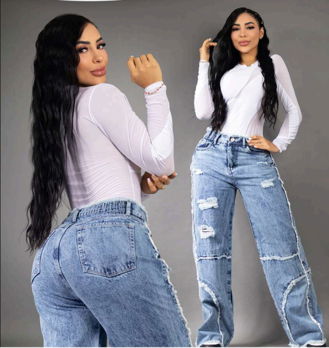 Modelo posando de frente y de espalda con jeans anchos tipo baggy en tono azul medio, con detalles de rotos en las rodillas, flecos and tiro alto, resaltando la silueta colombiana.