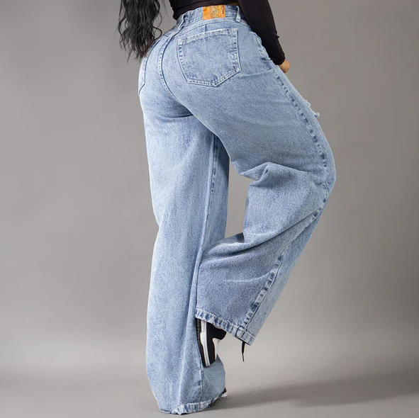 Modelo posando de frente con jeans anchos tipo baggy en tono azul medio, con detalles de rotos en las piernas y tiro alto, resaltando la silueta colombiana.