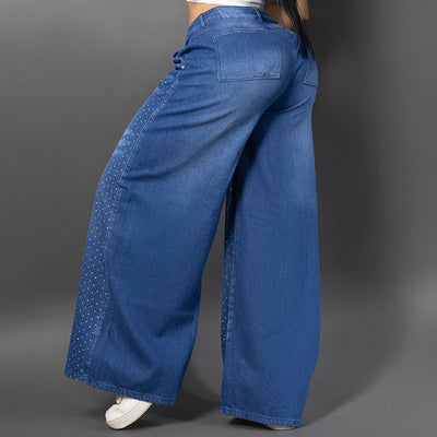 Vistas de lado de una modelo luciendo jeans baggy con un patrón de brillos horizontales en ambas piernas y un parche decorativo brillante. Ancho.