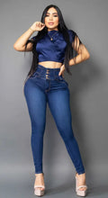 Modelo de lado luciendo jean colombiano azul Vengi Fit con detalle de doble cadena dorada en la cadera, pretina ancha y efecto levanta cola.